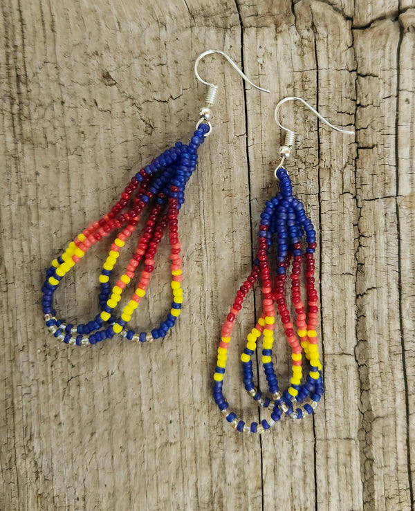 Shoshone-crafted dark blue dangly beaded loop earrings with red and yellow accents on rustic wood background