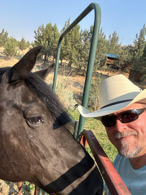 “Corey Rudolph in cowboy hat and sunglasses, standing in front of horse, carrying on Double R Western tradition.”
