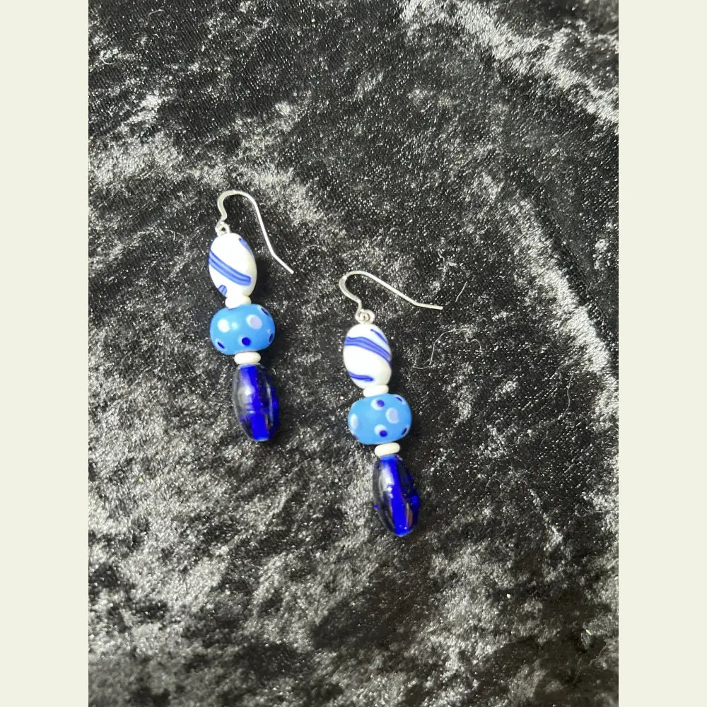 One-of-a-kind earrings by Amie Loiselle featuring blue and white antique glass trade beads, bone spacers, and sterling silver hooks on a black velvet background.
