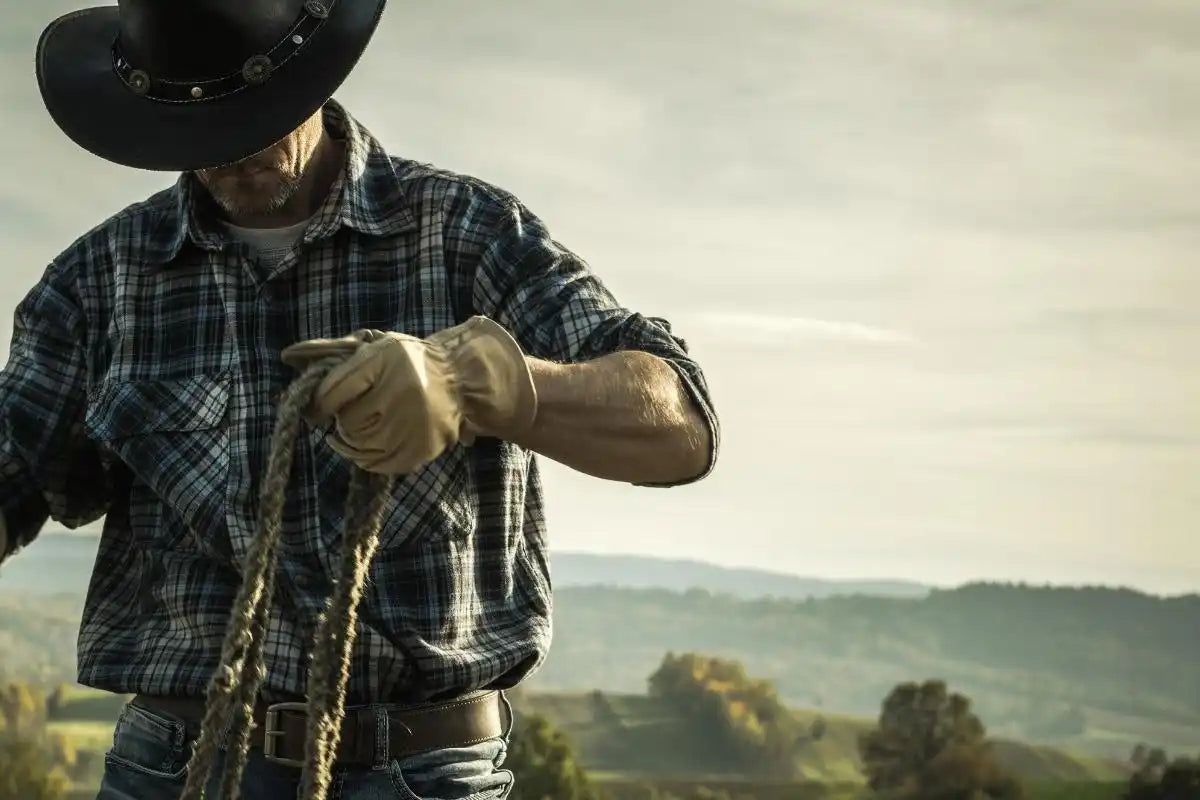 A cowboy in a plaid shirt and gloves, holding a rope.