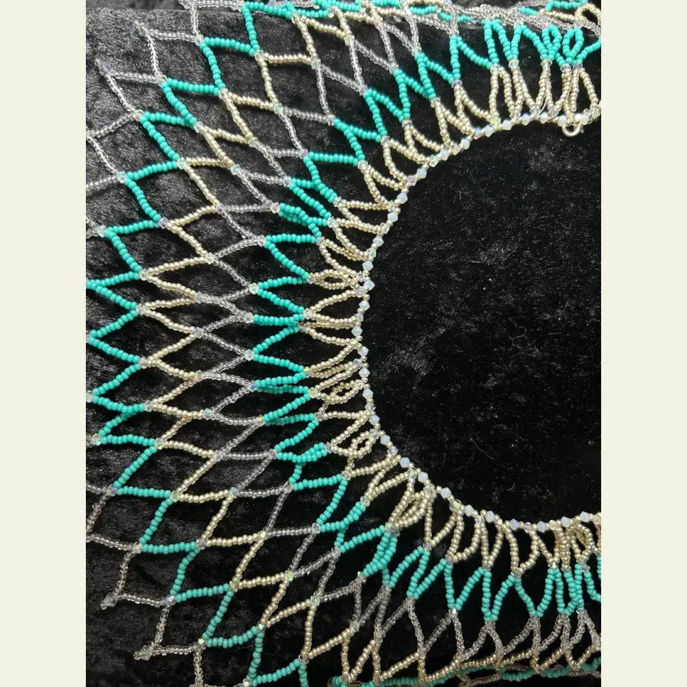 Handwoven seed bead and cut crystal collar necklace by artisan Amie Loiselle, featuring turquoise, silver, and iridescent beads on a black velvet background.