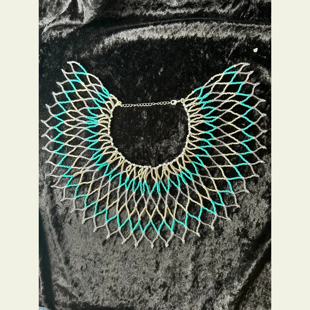 Handwoven seed bead and cut crystal collar necklace by artisan Amie Loiselle, featuring turquoise, silver, and iridescent beads on a black velvet background.