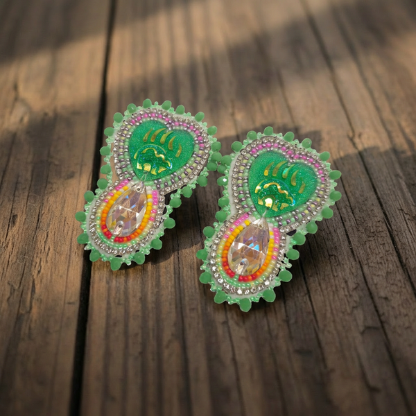 Hand-beaded green statement earrings with teardrop crystal drops on a wooden surface.