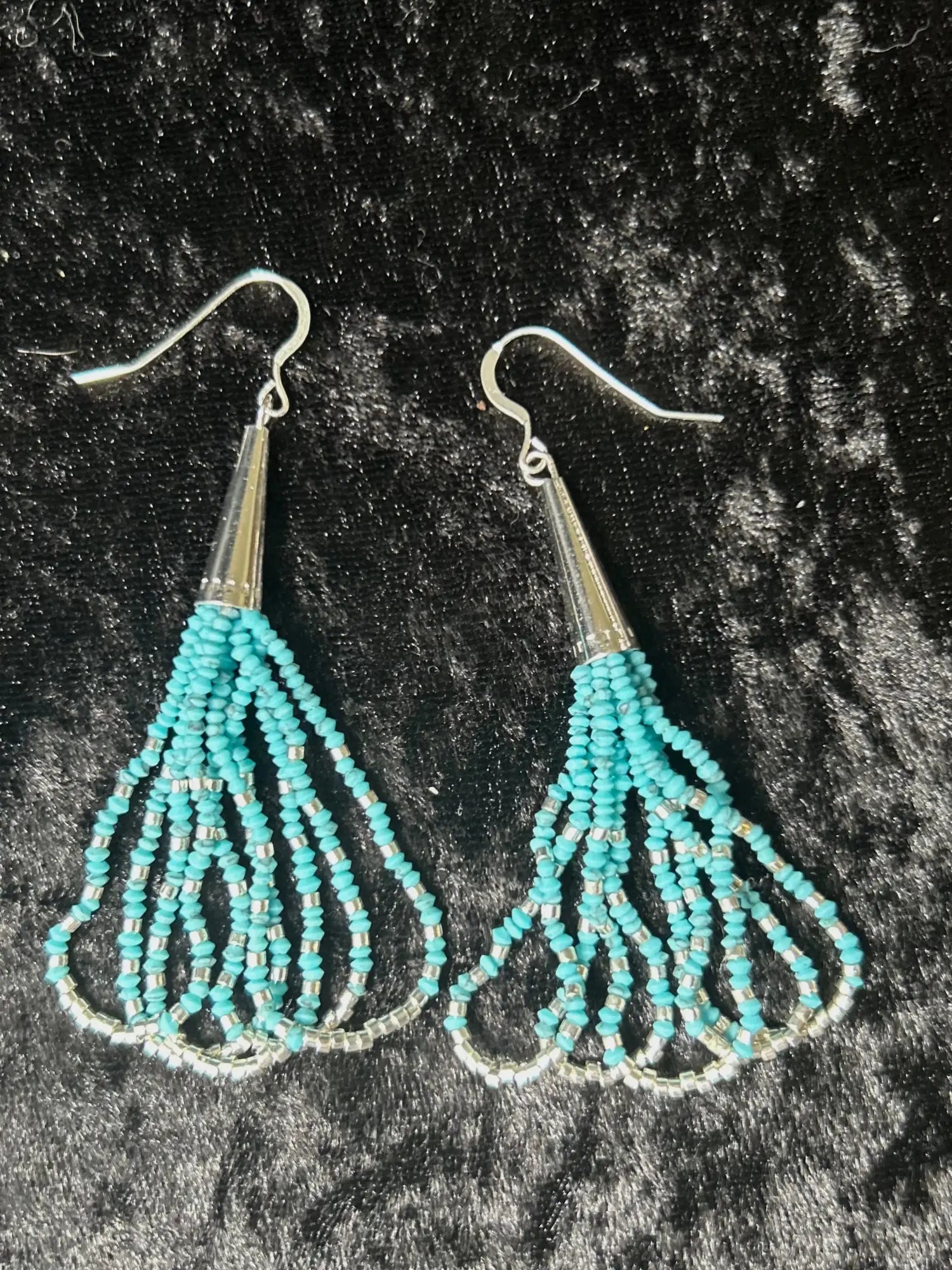 Handcrafted turquoise and silver-plated Sky Dance dangle earrings by Native Cherokee beadwork artist Amie Loiselle, displayed on a black velvet background.