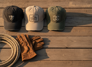 Three distressed dad hats arranged on weathered wood with western textures in warm light.