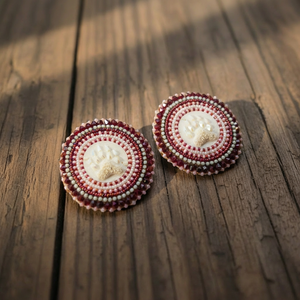 Close-up of handcrafted bear claw beaded earrings featuring a detailed bear claw centerpiece surrounded by concentric rows of pink, burgundy, and pearl beads, photographed on a natural wood background.