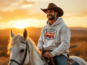  Man wearing a heritage men’s hoodie and cowboy hat, riding a white horse at sunset
