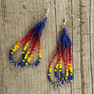 Shoshone-crafted dark blue dangly beaded loop earrings with red and yellow accents on rustic wood background