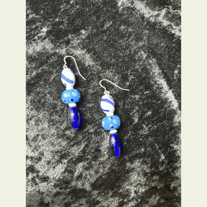 
One-of-a-kind earrings by Amie Loiselle featuring blue and white antique glass trade beads, bone spacers, and sterling silver hooks on a black velvet background.