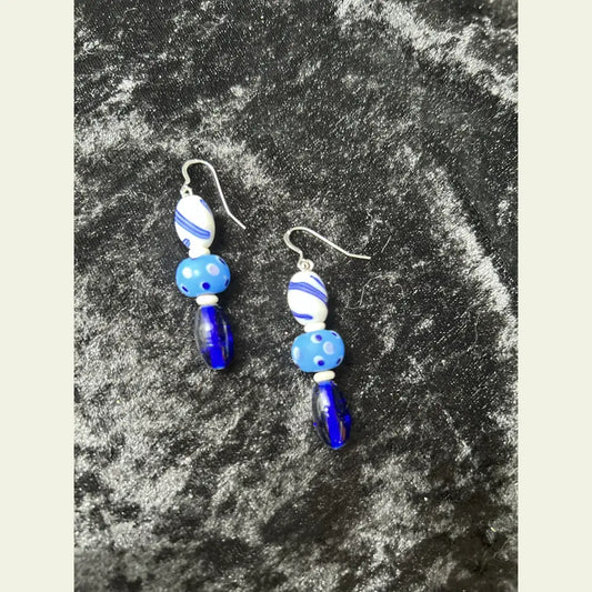 
One-of-a-kind earrings by Amie Loiselle featuring blue and white antique glass trade beads, bone spacers, and sterling silver hooks on a black velvet background.