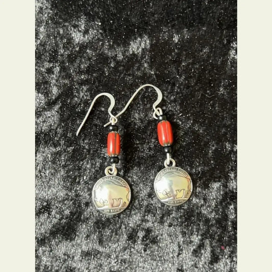 Limited edition earrings by Amie Loiselle featuring red and black trade beads with silver-plated buffalo nickel charms, displayed on a black velvet background.