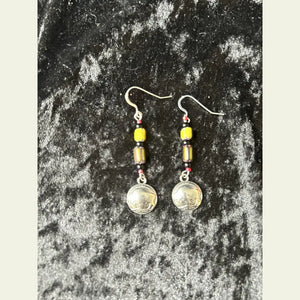 Double R Western exclusive earrings by Amie Loiselle featuring yellow and black trade beads with silver-plated buffalo nickel medallions, displayed on a black velvet background.