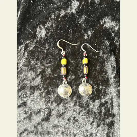 Double R Western exclusive earrings by Amie Loiselle featuring yellow and black trade beads with silver-plated buffalo nickel medallions, displayed on a black velvet background.