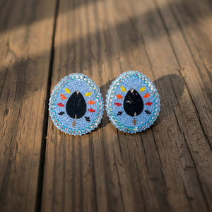 Hand-beaded blue oval stud earrings with black center stones on a wooden surface.