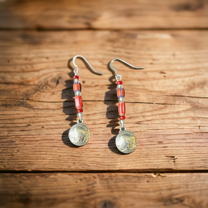 Double R Western exclusive earrings by Amie Loiselle featuring red and blue trade beads with silver-plated buffalo nickel charms, displayed on rustic wood background