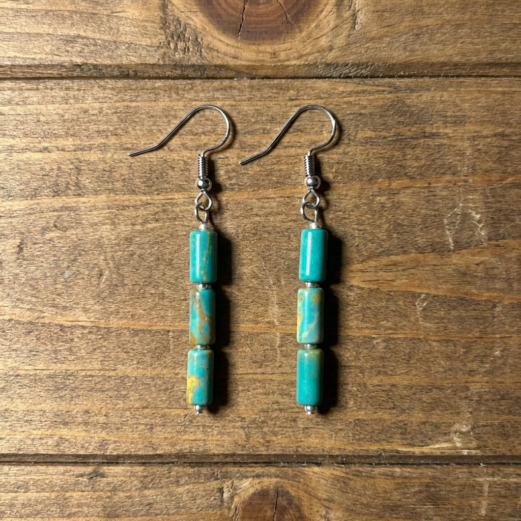 Handcrafted turquoise dangle earrings by artisan Amie Loiselle, featuring three genuine turquoise stones on each earring, displayed on a wood background