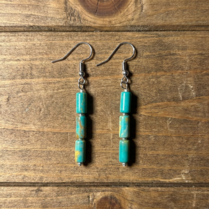 Handcrafted turquoise dangle earrings by artisan Amie Loiselle, featuring three genuine turquoise stones on each earring, displayed on a wood background