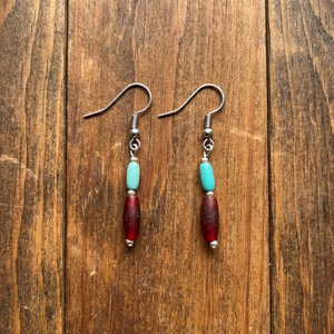 Handcrafted turquoise and red accent bead dangle earrings by artisan Amie Loiselle, displayed on a wood background.