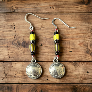 Double R Western exclusive earrings by Amie Loiselle featuring yellow and black trade beads with silver-plated buffalo nickel medallions, displayed on a wood background.