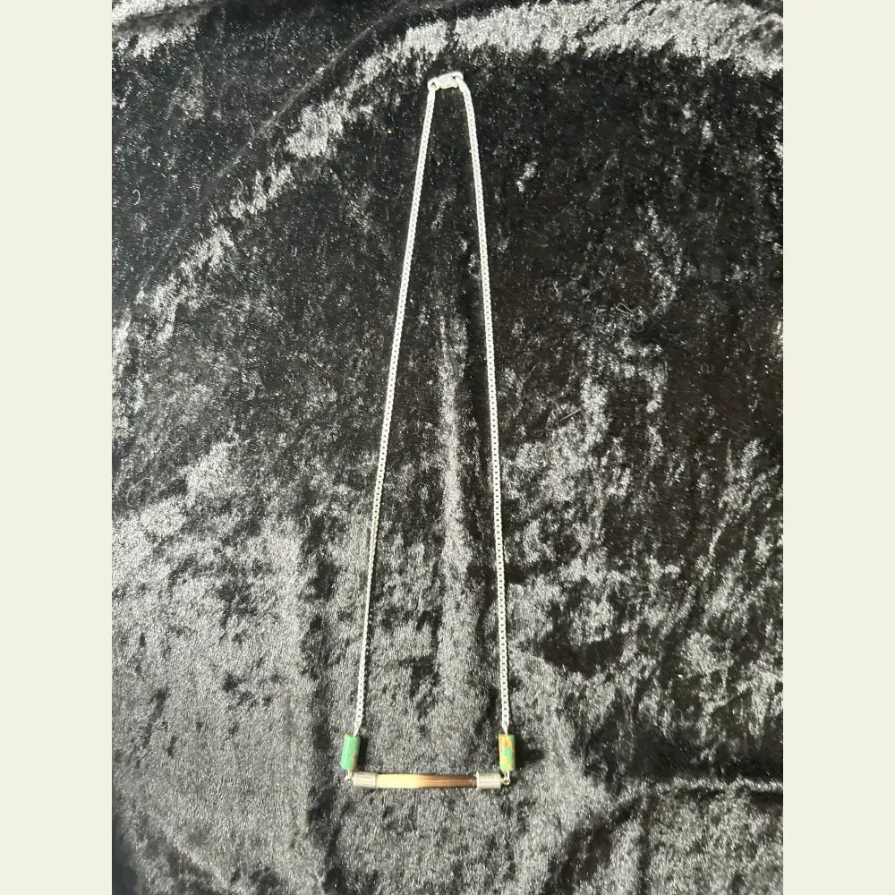 Handcrafted necklace featuring an African porcupine quill bar with turquoise beads on a sterling silver chain, displayed on a black velvet background.
