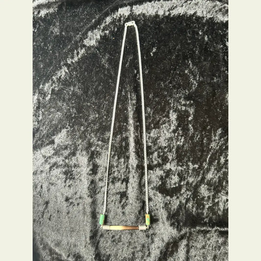 Handcrafted necklace featuring an African porcupine quill bar with turquoise beads on a sterling silver chain, displayed on a black velvet background.
