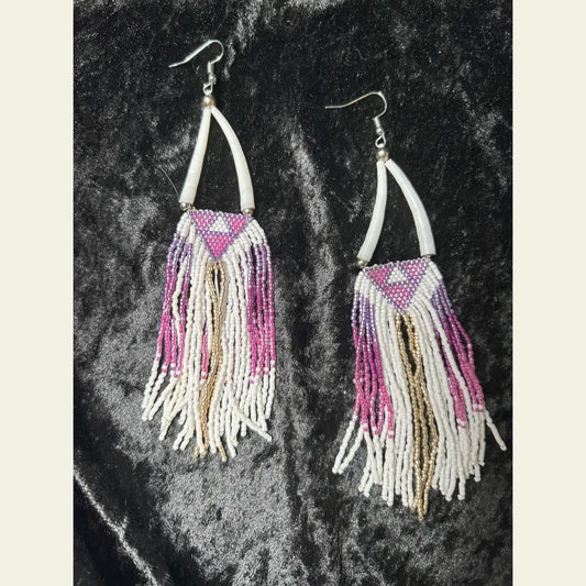 One-of-a-kind long beaded fringe earrings by Amie Loiselle, featuring pink, purple, gold, and white seed beads with shell accents on silver-plated hooks, displayed on a black velvet background.