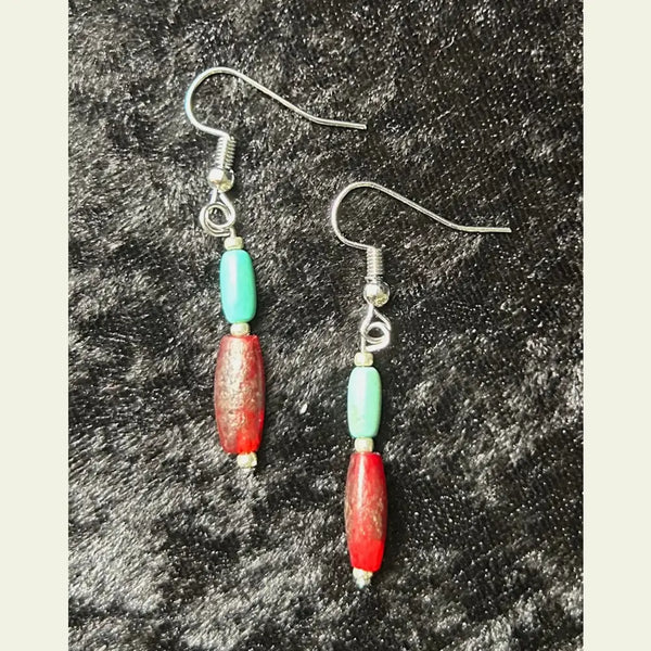 Handcrafted turquoise and red accent bead dangle earrings by artisan Amie Loiselle, displayed on a black velvet background.