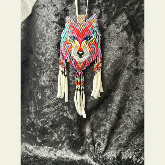 Handcrafted Spirit Wolf medallion necklace by Amie Loiselle, featuring colorful glass and seed beadwork with dentalium shell fringe on a ribbon, displayed on black velvet.