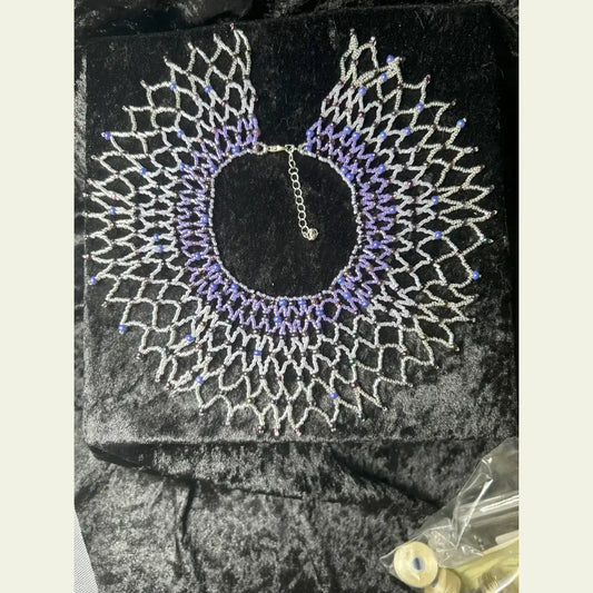 Handwoven small collar necklace by Amie Loiselle, featuring a netted design with glass and seed beads in purple and silver tones, displayed on a black velvet background.
